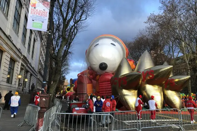 The big character balloons of Astronaut Snoopy, under a net plus smaller golden Macy's star balloons, await at the start of the parade.